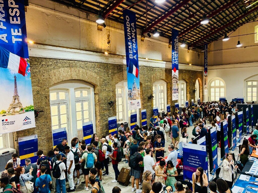 Elevated view of the 'Bem-vindo à França' pavilion with Eiffel Tower banners and large student turnout